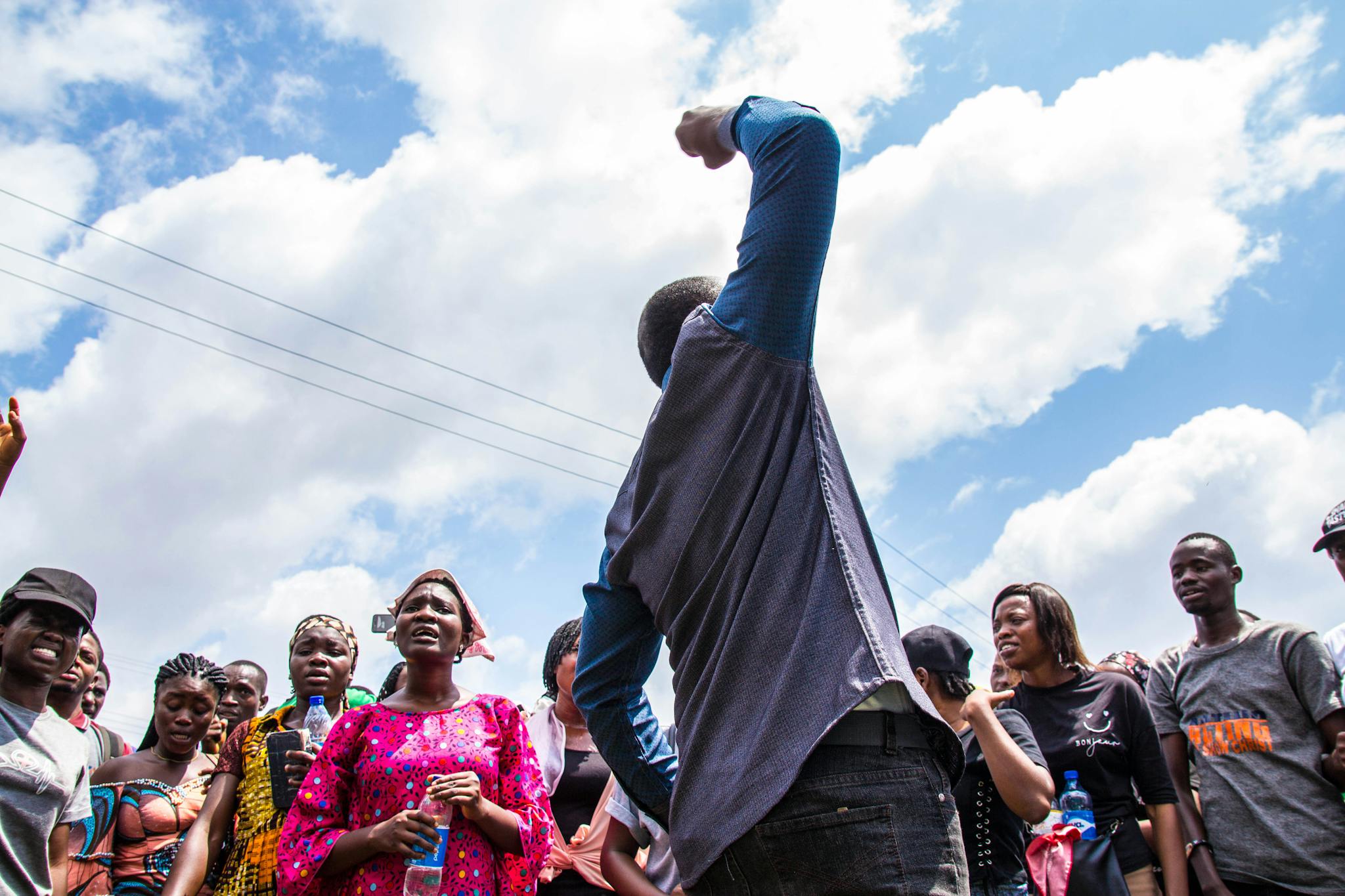 A diverse group of people engaged in an outdoor protest with raised voices and arms, displaying unity and motivation.